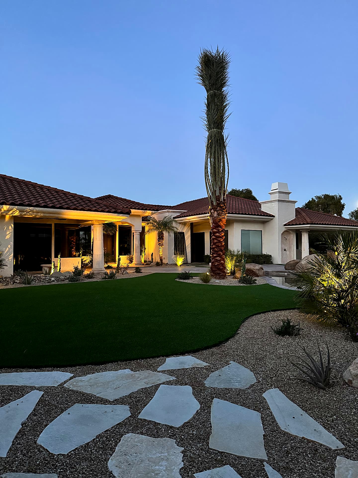 Twilight backyard with an uplit palm, flagstone path and warm garden lighting