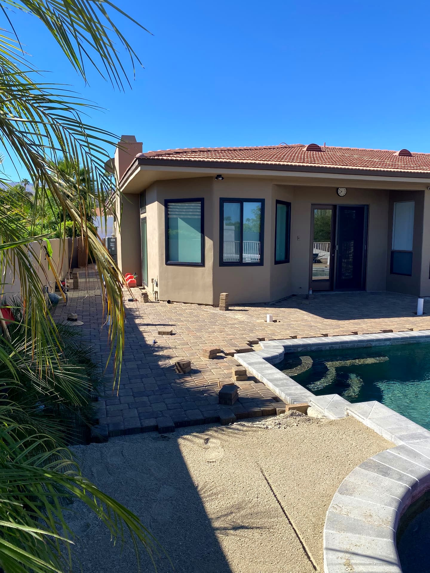 During installation — paver pool deck in progress beside the pool with coping set in place